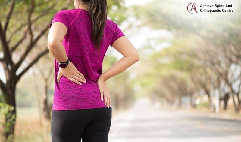 Athlete clutching her lower back in pain while jogging outdoors.