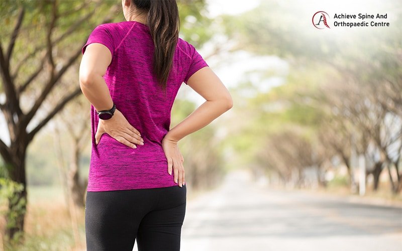 Athlete clutching her lower back in pain while jogging outdoors.
