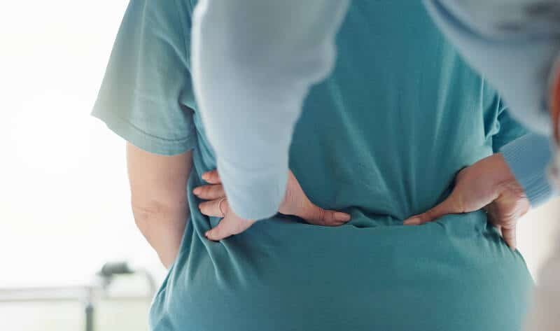 Patient holding lower back experiencing persistent post-fusion spine pain.