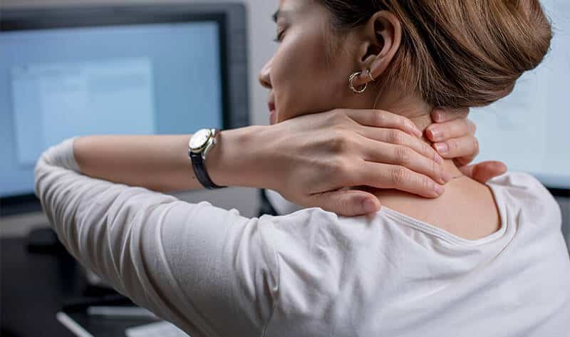 Person holding neck at computer desk.